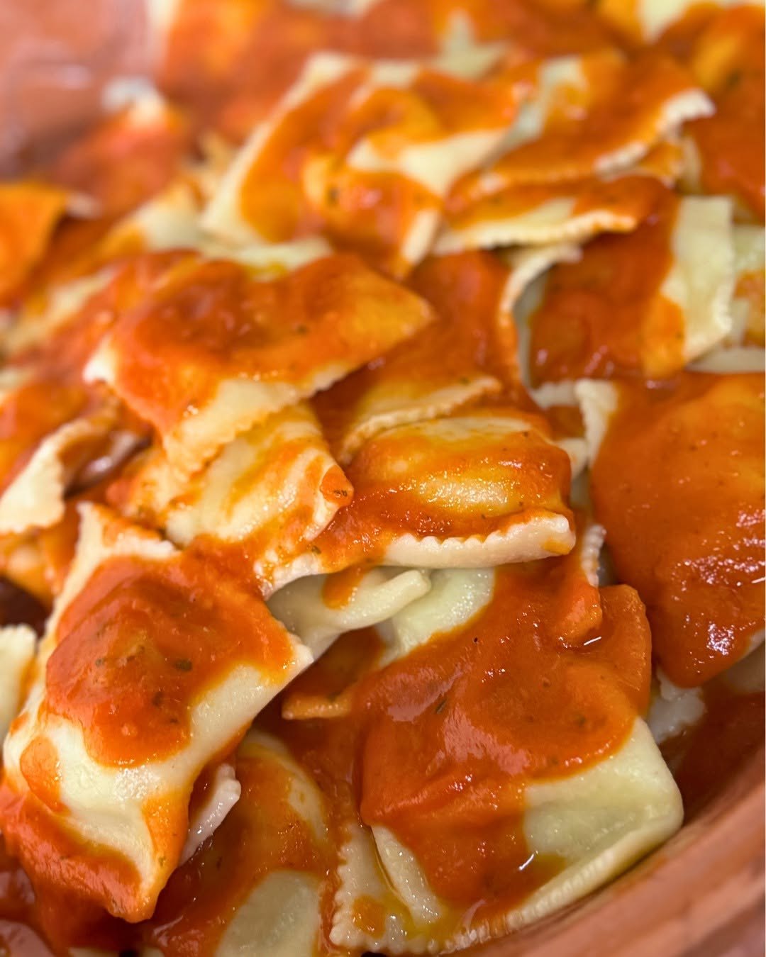 Ravioli ripieni dai bordi dentellati con sugo di pomodoro in una ciotola di terracotta, fatti a mano da Agriturismo Gutturus
