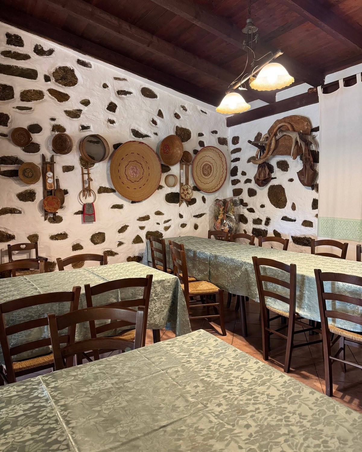 Sala dell'Agriturismo Gutturus: muri in pietra, travi scure, cesti intrecciati appesi e tavoli con tovaglie verdi